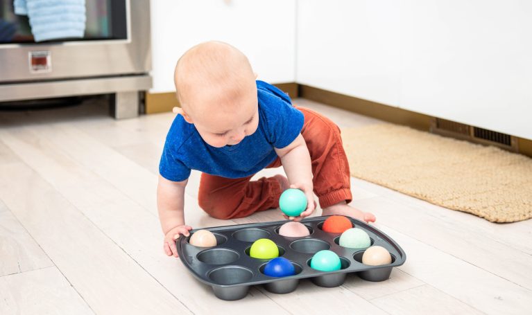 Baby playing with balls in a muffin tin
