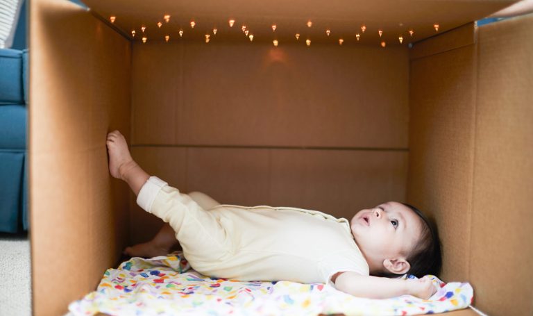 Baby laying in a cardboard box looking up at lights