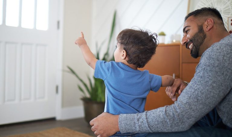 Man supporting a child who is pointing out the front door