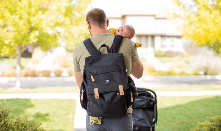 Man holding a baby wearing a backpack