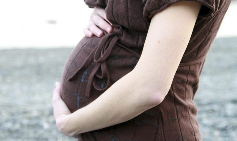 A mother cradles her pregnant belly in her arms.
