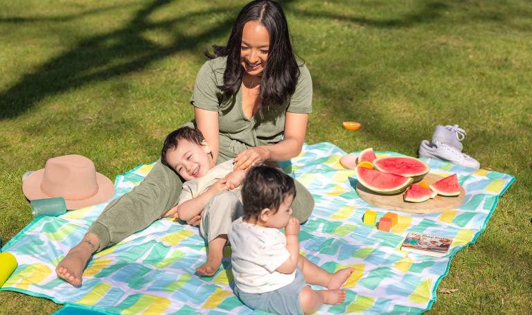Mother sits with her children on a picnic blanket.