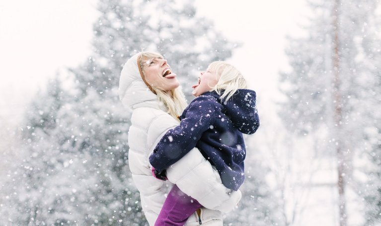 Mother collects snowflakes on her tongue with her daughter.