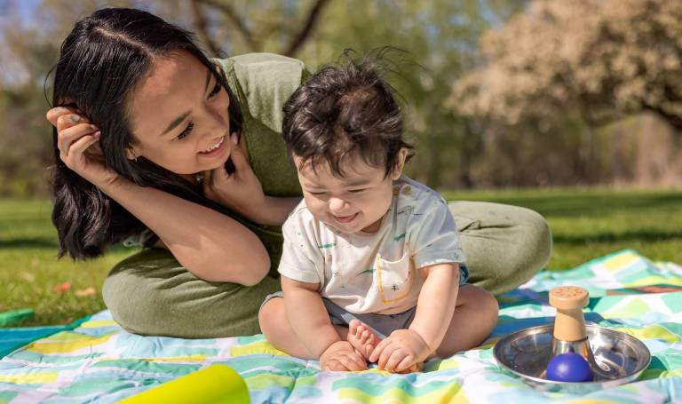 Mom talks to her baby on a picnic blanket.