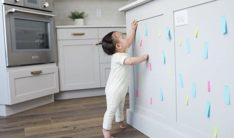 Toddler taking sticky notes off a wall