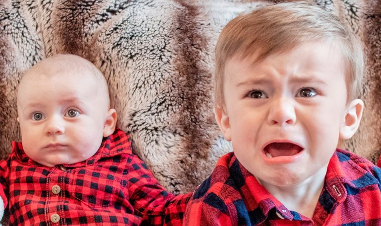 A baby and an upset young child wearing matching red shirts