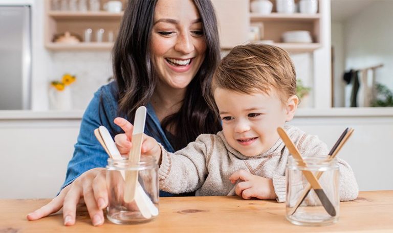 Toddler sitting in a woman's lap looking at two canisters filled with wooden popsicle sticks