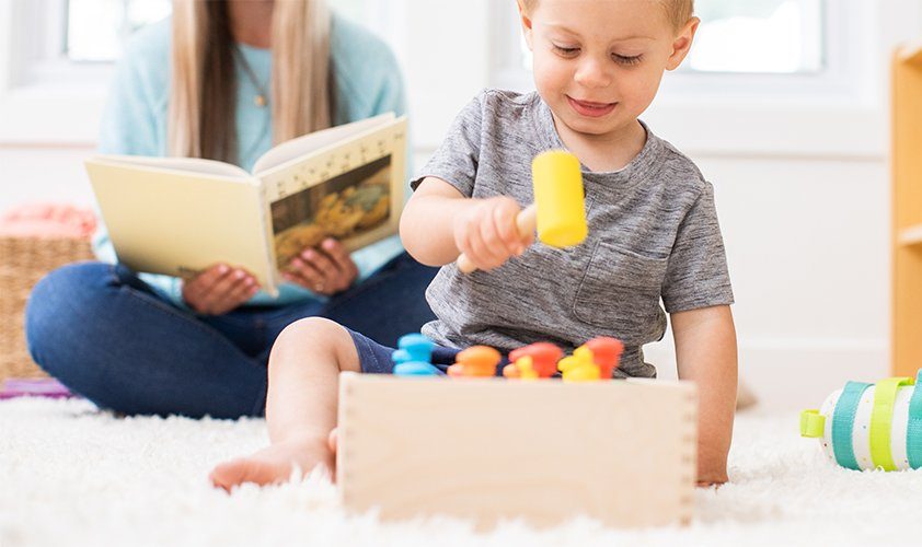 Toddler playing with a hammer wooden toy while sitting on the ground