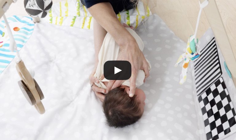 Woman helping a newborn do tummy time under The Play Gym by Lovevery