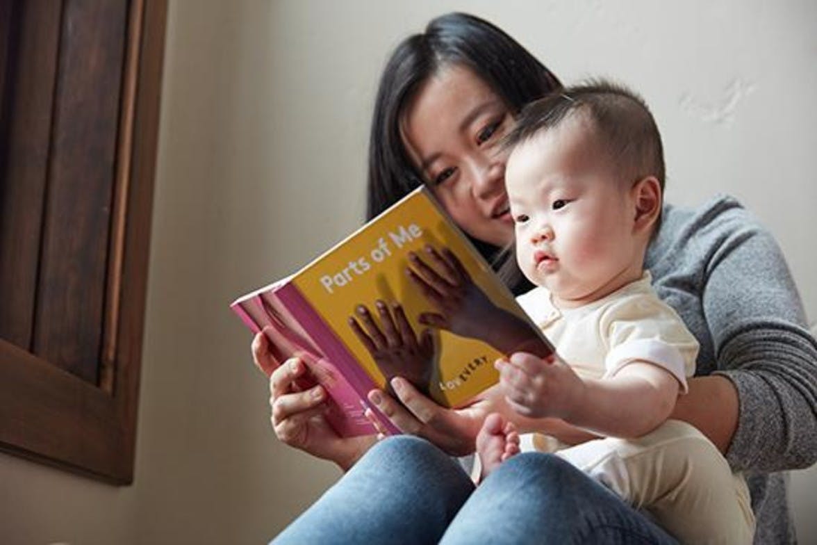 Woman holding a baby in their lap while looking at a book about body parts by Lovevery.