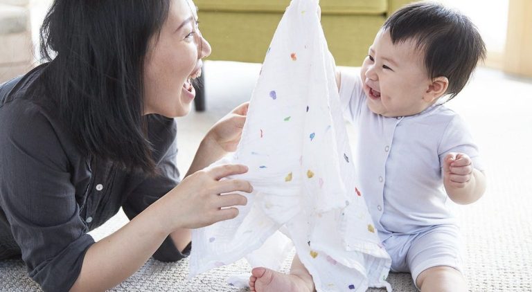 Woman and baby smiling and playing with an organic swaddle by Lovevery