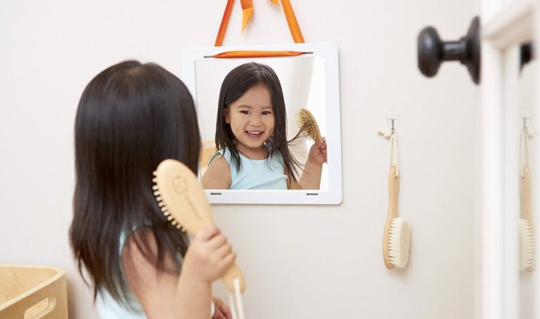 Young child looking at themselves in a mirror while brushing their hair