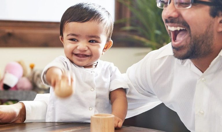 Baby sitting up and playing with a wooden ball and cup