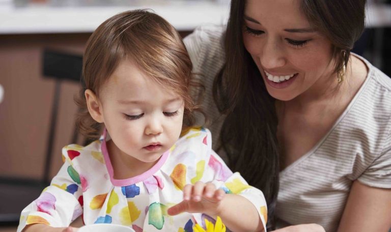 Toddler sitting on a woman's lap looking at her hand