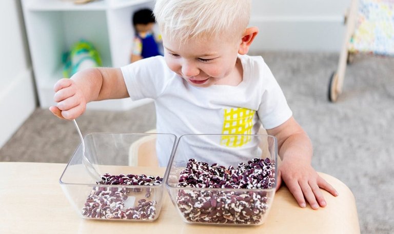 Toddler scooping dried beans from one bowl to another using a spoon