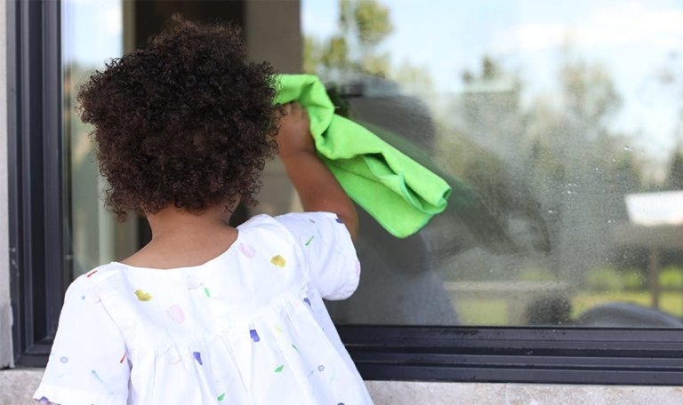 Young child holding a rag and cleaning a window