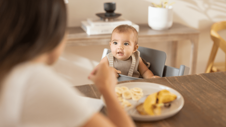 Mother and baby share food at the table.